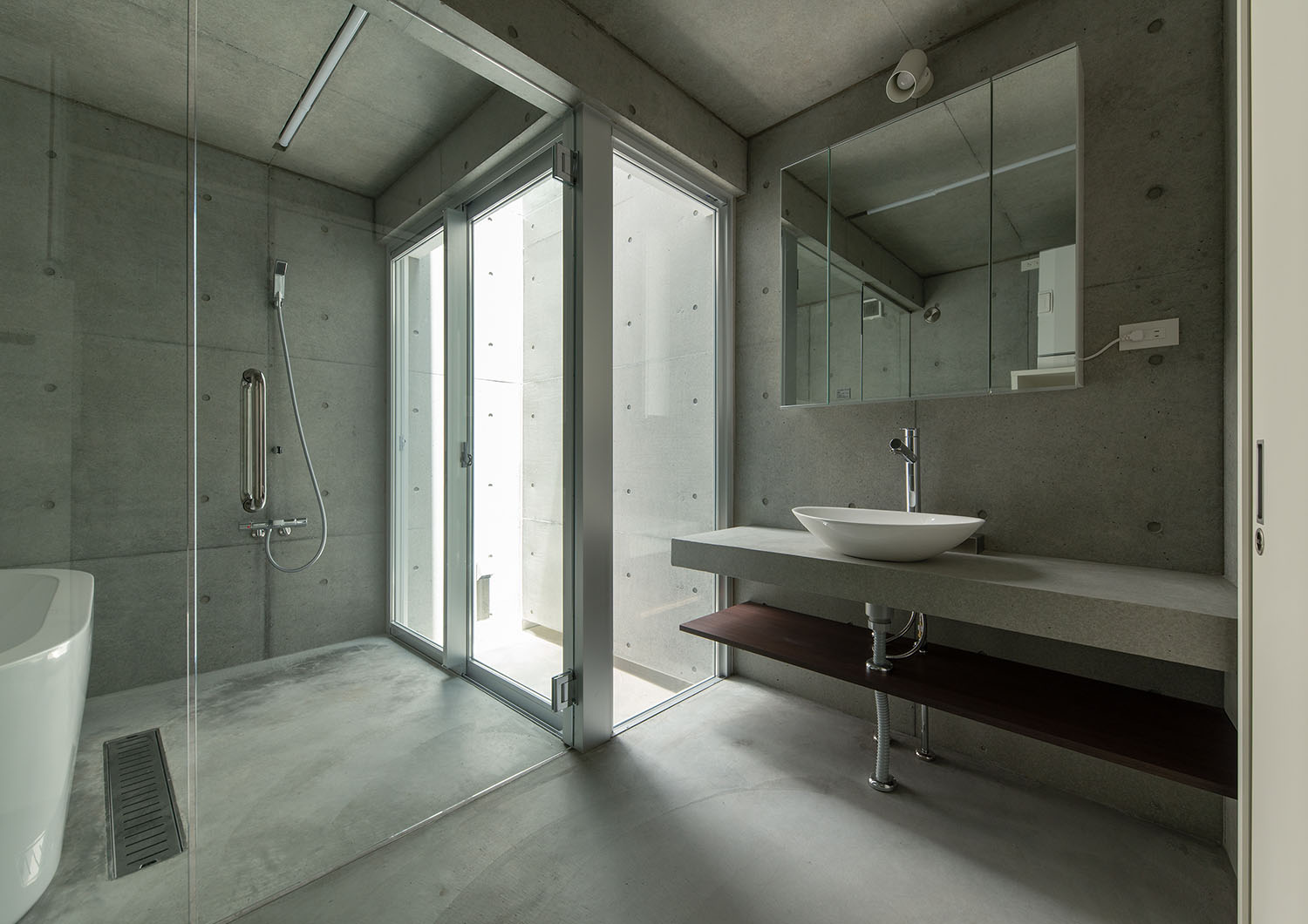 ガラス扉で仕切られているコンクリート壁の洗面所と浴室・デザイン住宅
