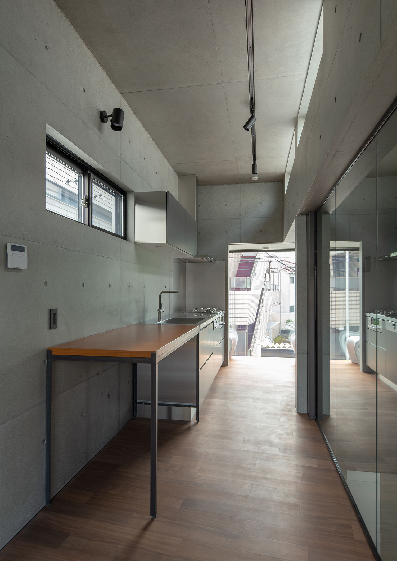 コンクリートの壁の空間の隅にキッチンと木のテーブルがある・デザイン住宅