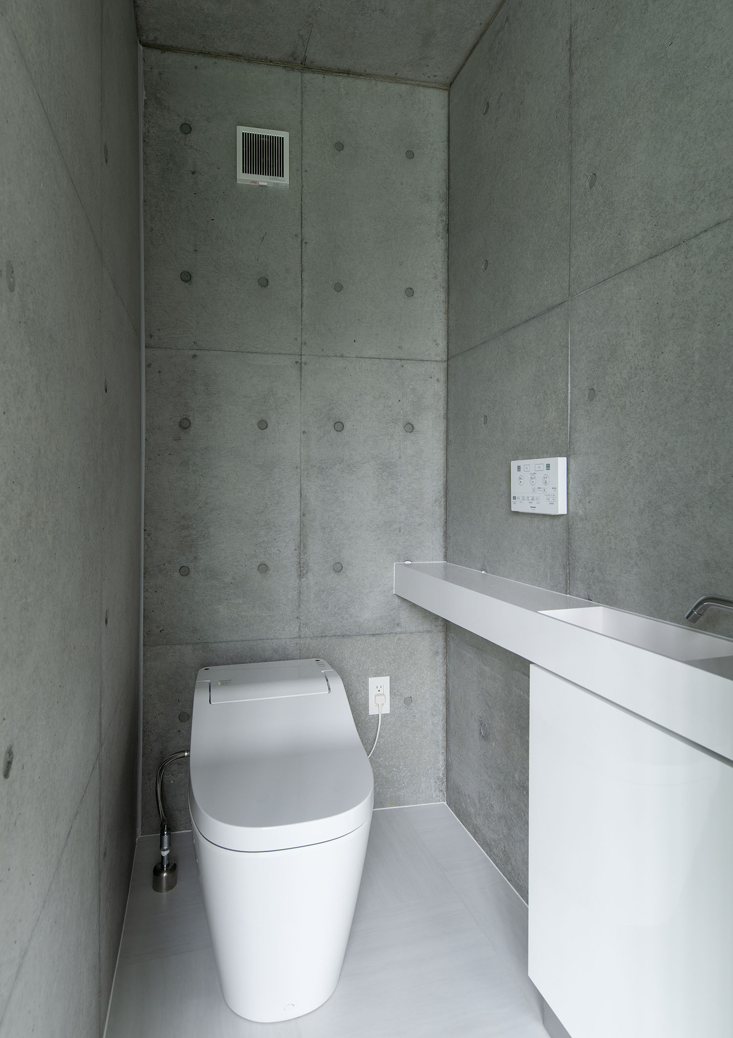 コンクリート壁に囲まれた薄型手洗いのあるトイレ・デザイン住宅