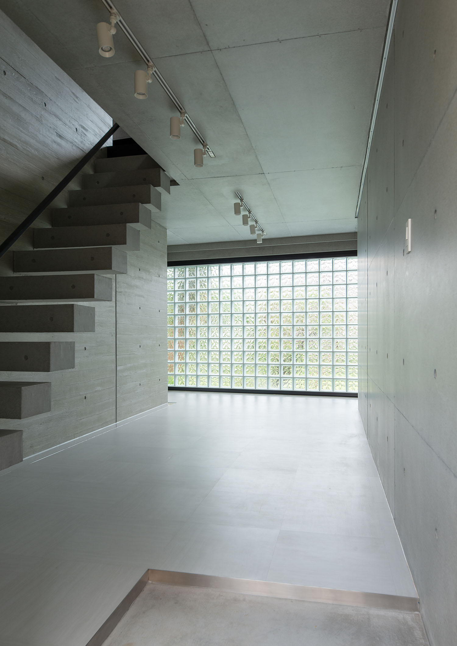 壁と階段がコンクリ―トになっており、一面がガラスブロックの壁になっている空間・デザイン住宅