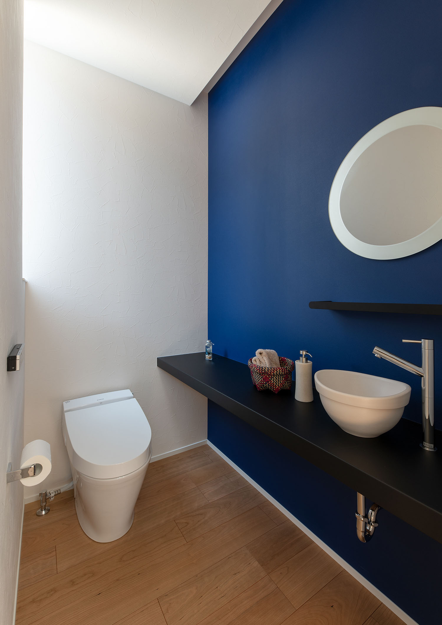 丸い鏡や薄型手洗いがある、青いアクセントクロスのトイレ・デザイン住宅