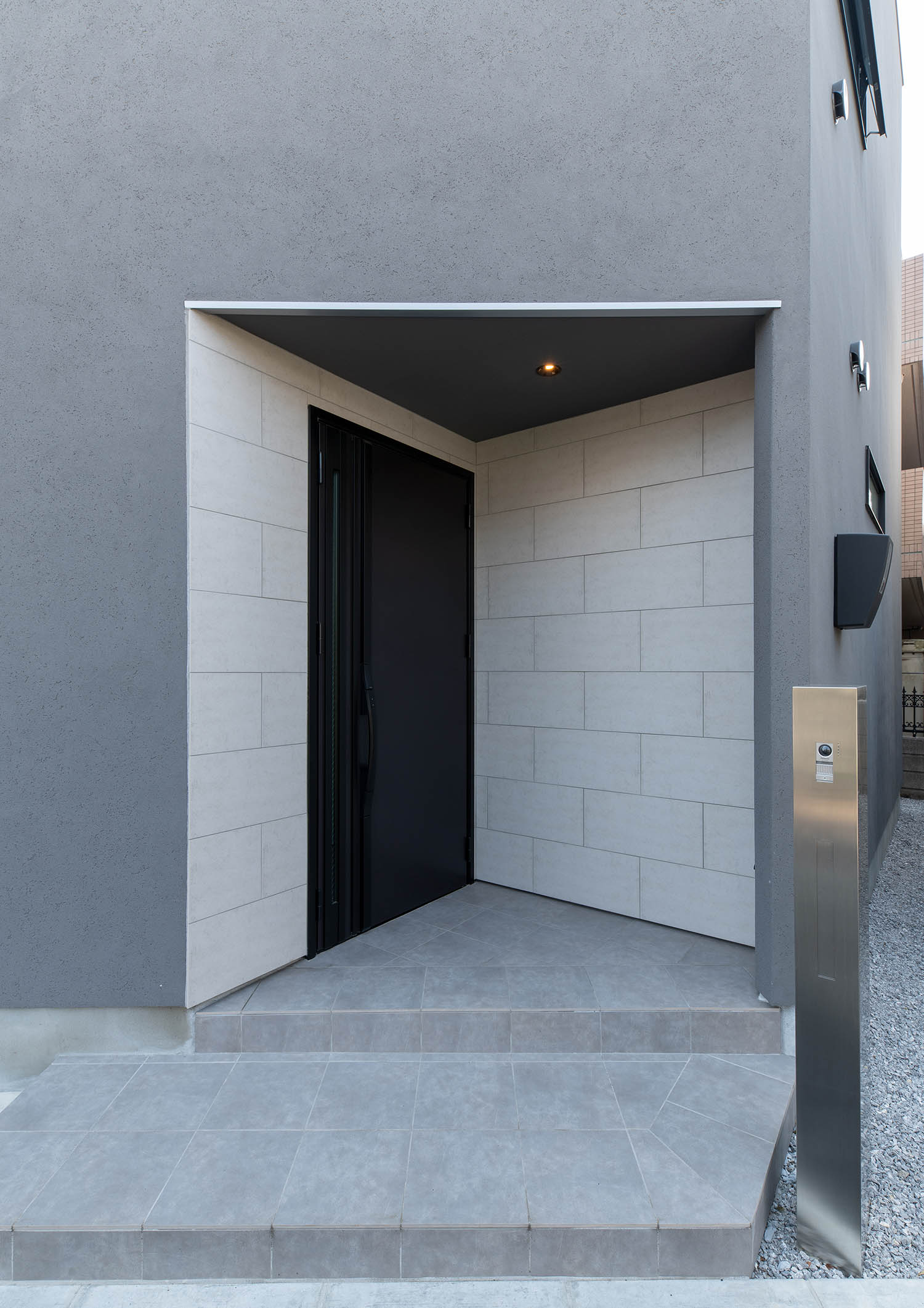 タイル張りの壁に黒い玄関扉が付けられた玄関ポーチ・デザイン住宅
