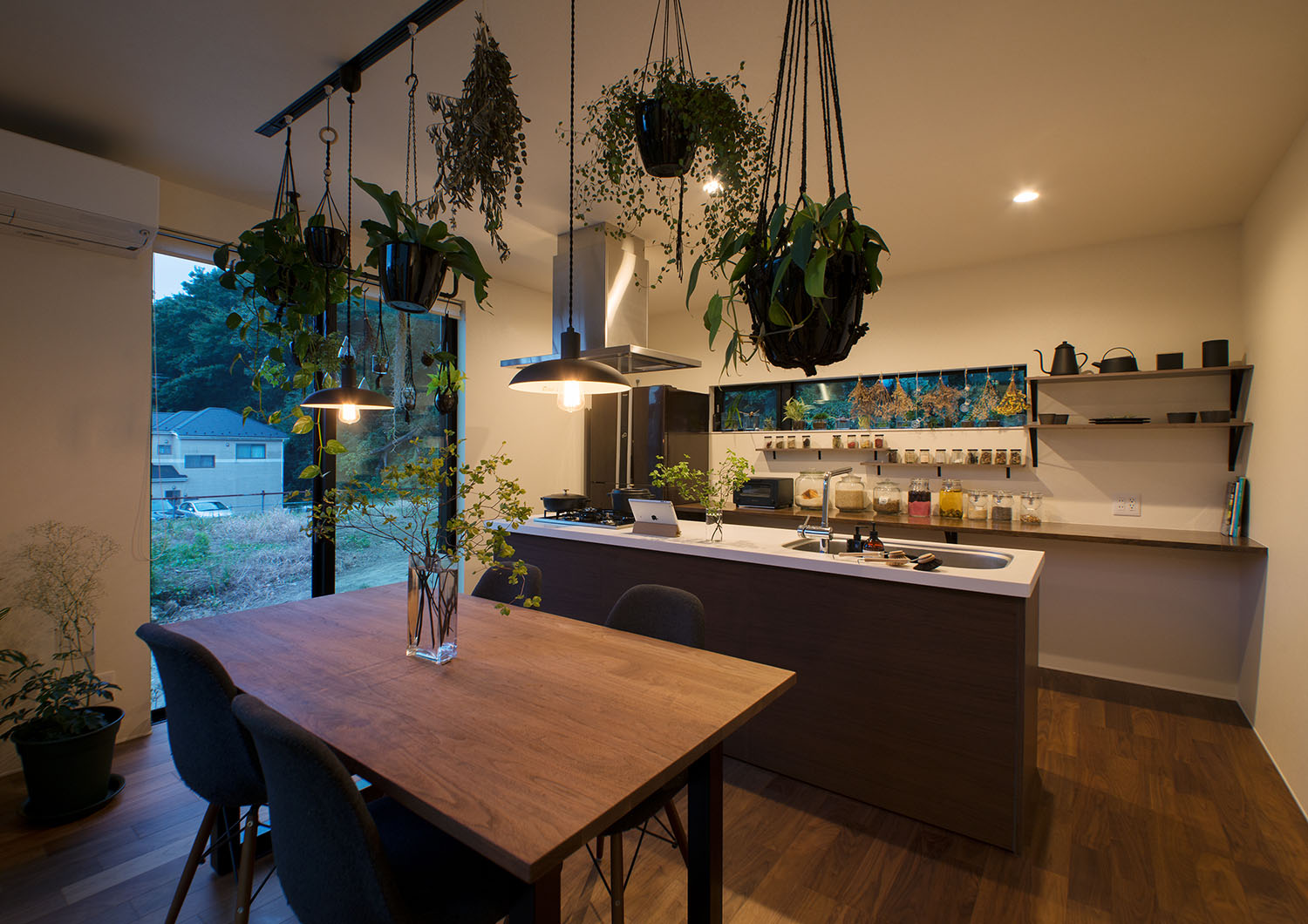 観葉植物と並べて天井から吊り下げられたペンダントライトがあるダイニング・デザイン住宅