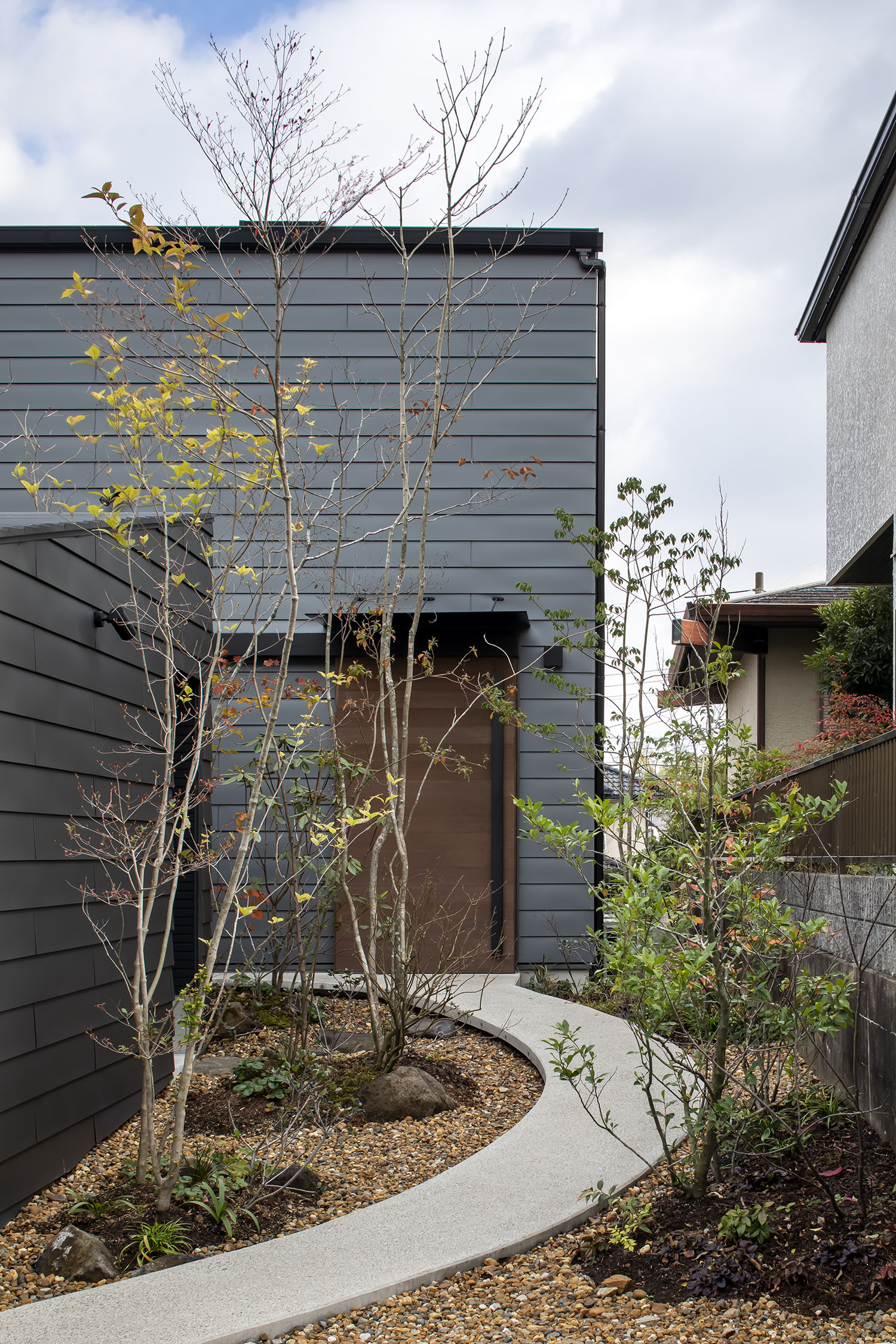 植栽のあるアプローチの先に見える、木の扉がついた住宅・デザイン住宅