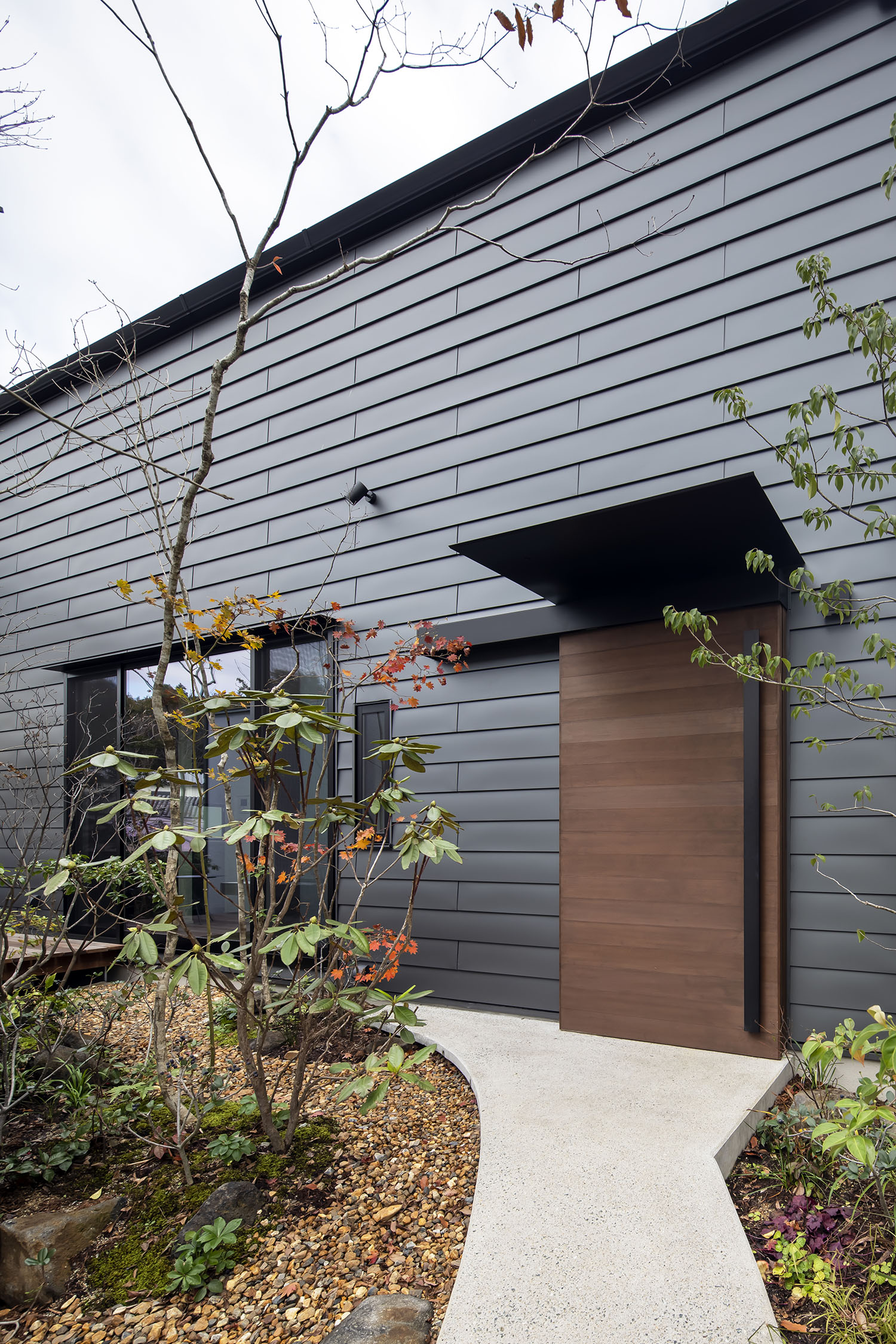 黒い外壁に木の扉がついた住宅の回りに植栽がある様子・デザイン住宅