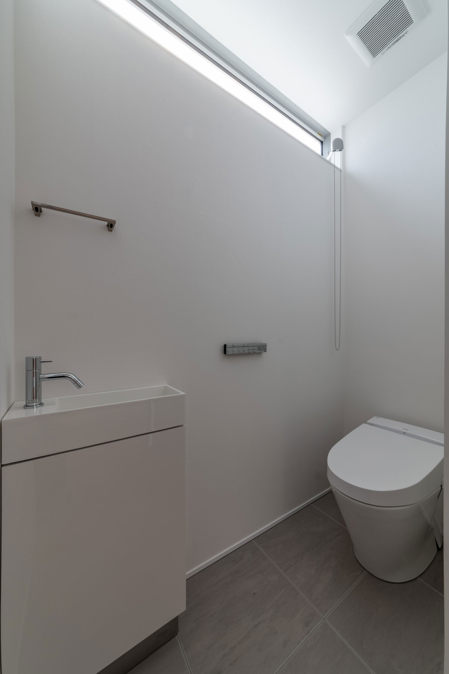 白を基調とした、スリット窓と薄型手洗いのあるトイレ・フリーダムアーキテクツの事例