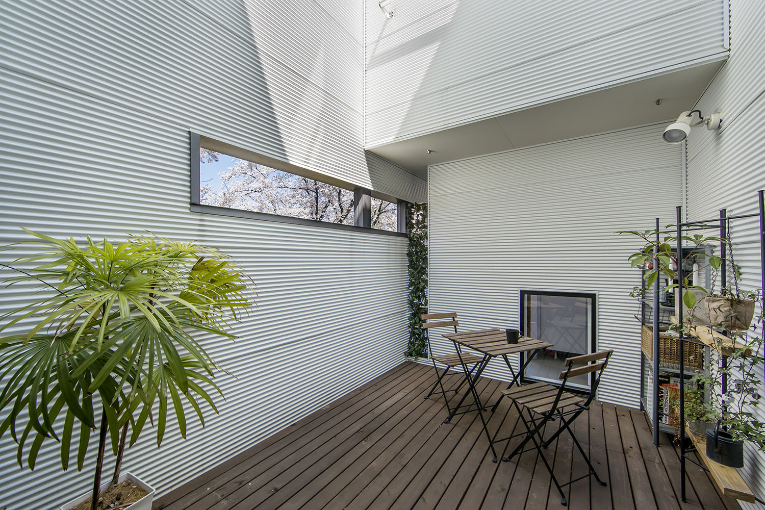 白い壁に囲まれた、スリット窓のあるウッドデッキの中庭・フリーダムアーキテクツの事例