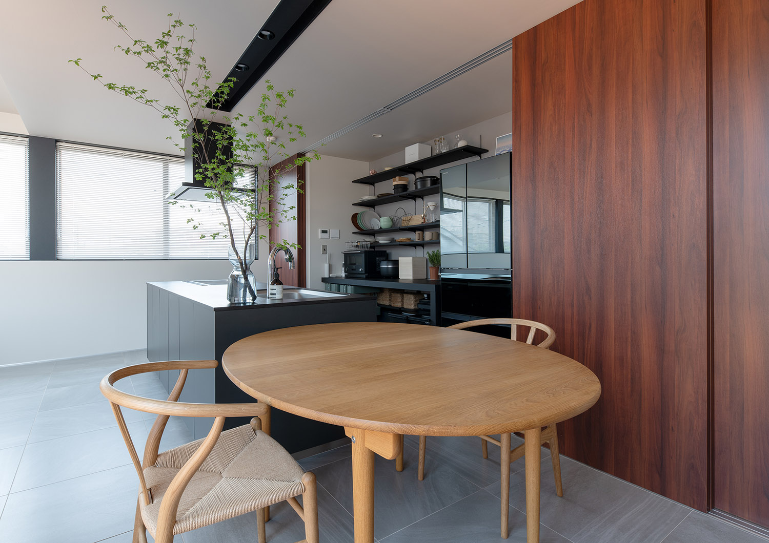 木の丸いテーブルが黒いアイランドキッチンの横に並べられている・フリーダムアーキテクツの事例