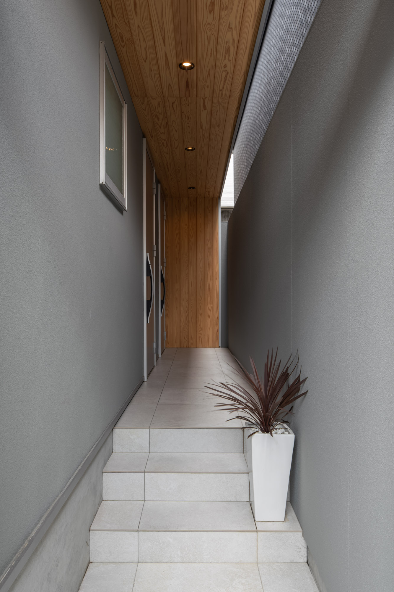 木の軒天井があり、白いタイル張りの階段を上がる玄関アプローチ・デザイン住宅