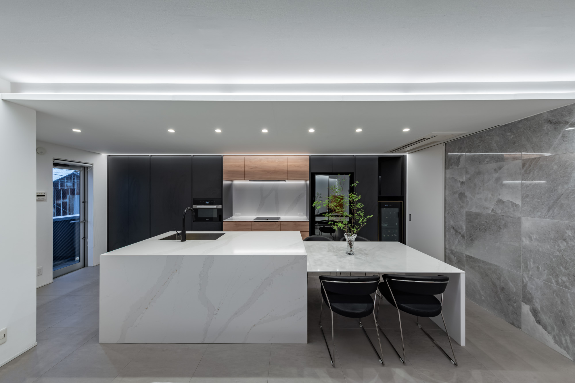 天井に段差を設け、間接照明を仕込んだ空間にある、ダイニングテーブルが一体となった大理石風のキッチン・デザイン住宅