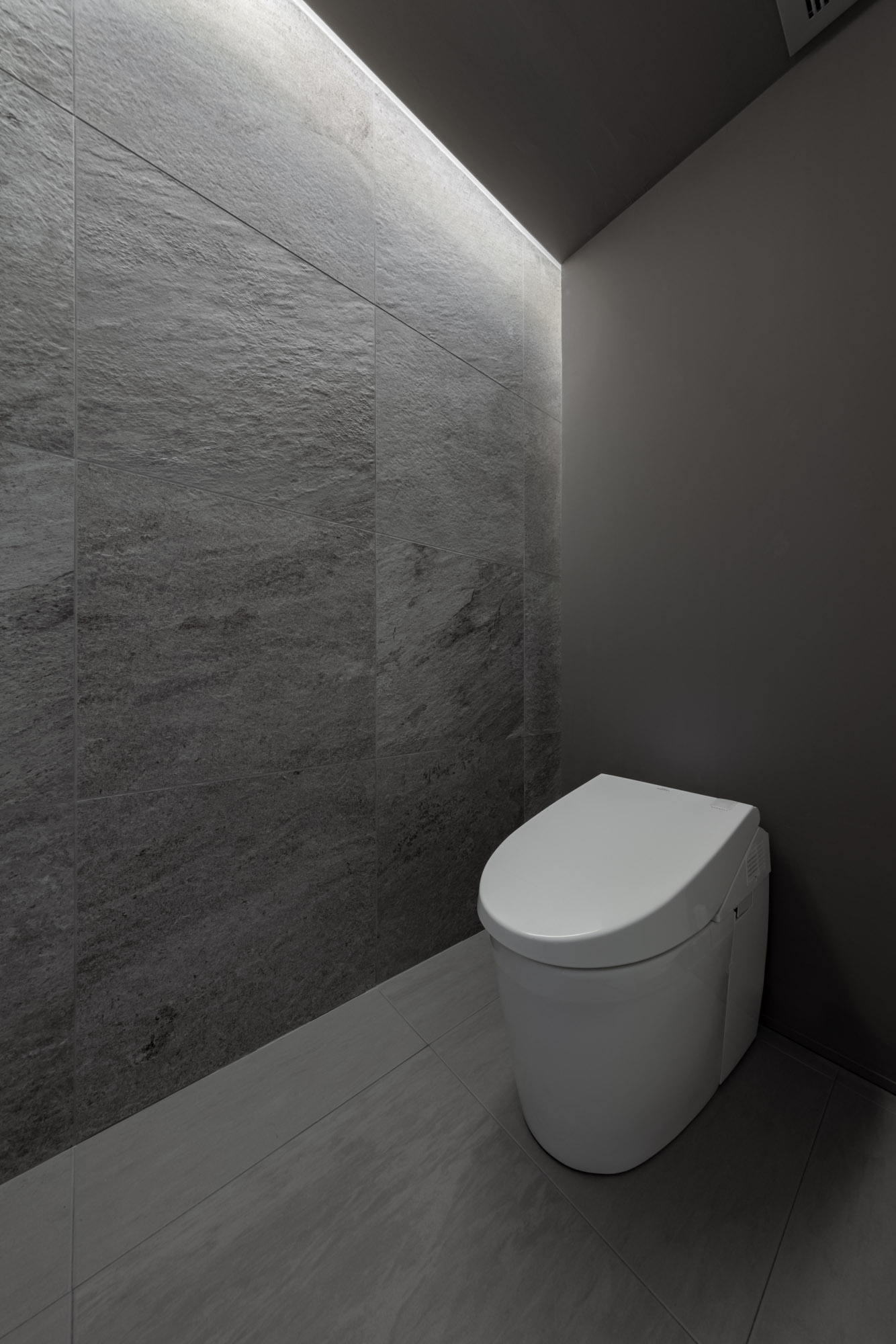 壁紙をグレーで統一し、間接照明をもうけたタンクレスのトイレがある空間・デザイン住宅