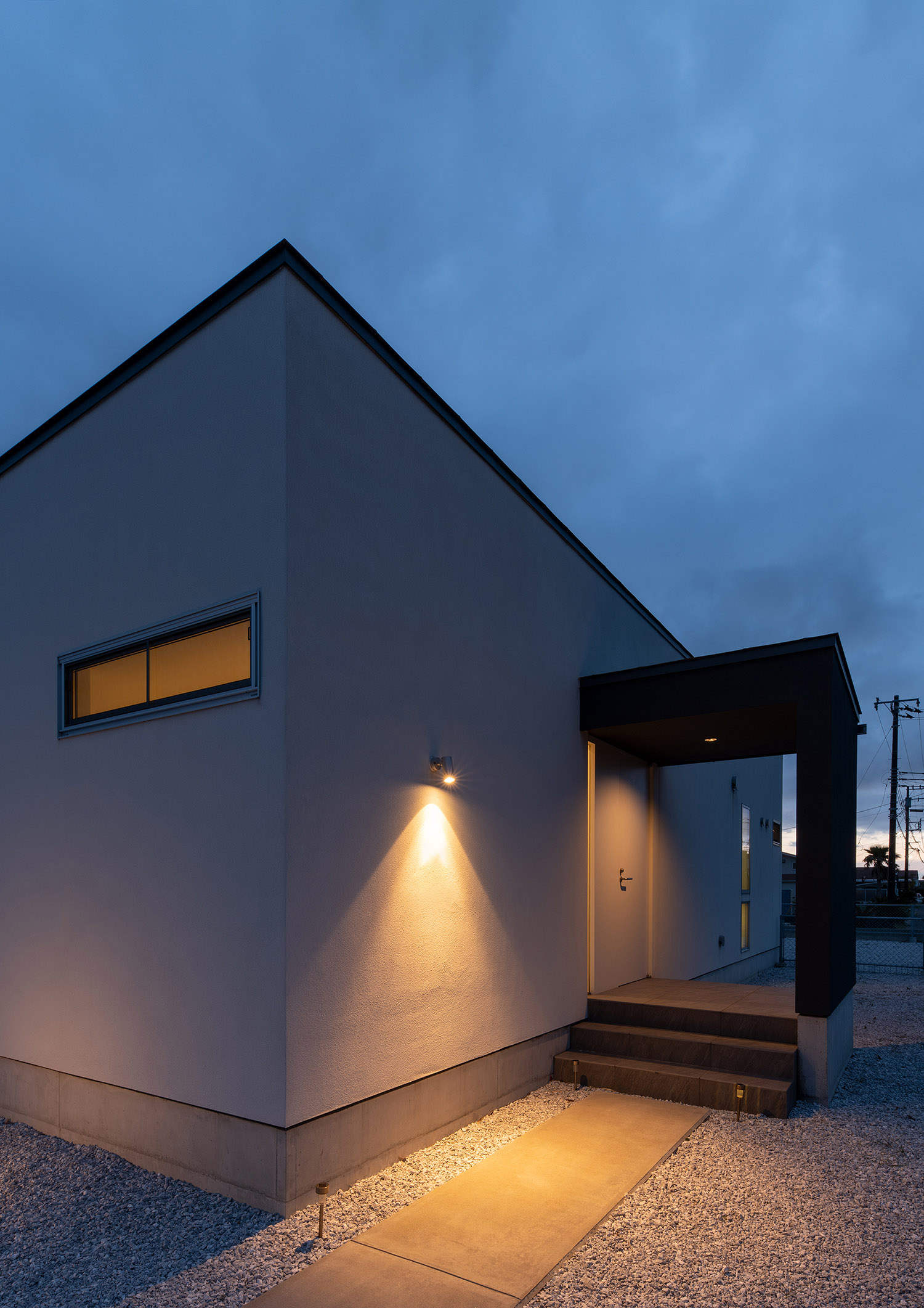 外壁に取り付けられた屋外照明が玄関アプローチを照らしている様子・デザイン住宅