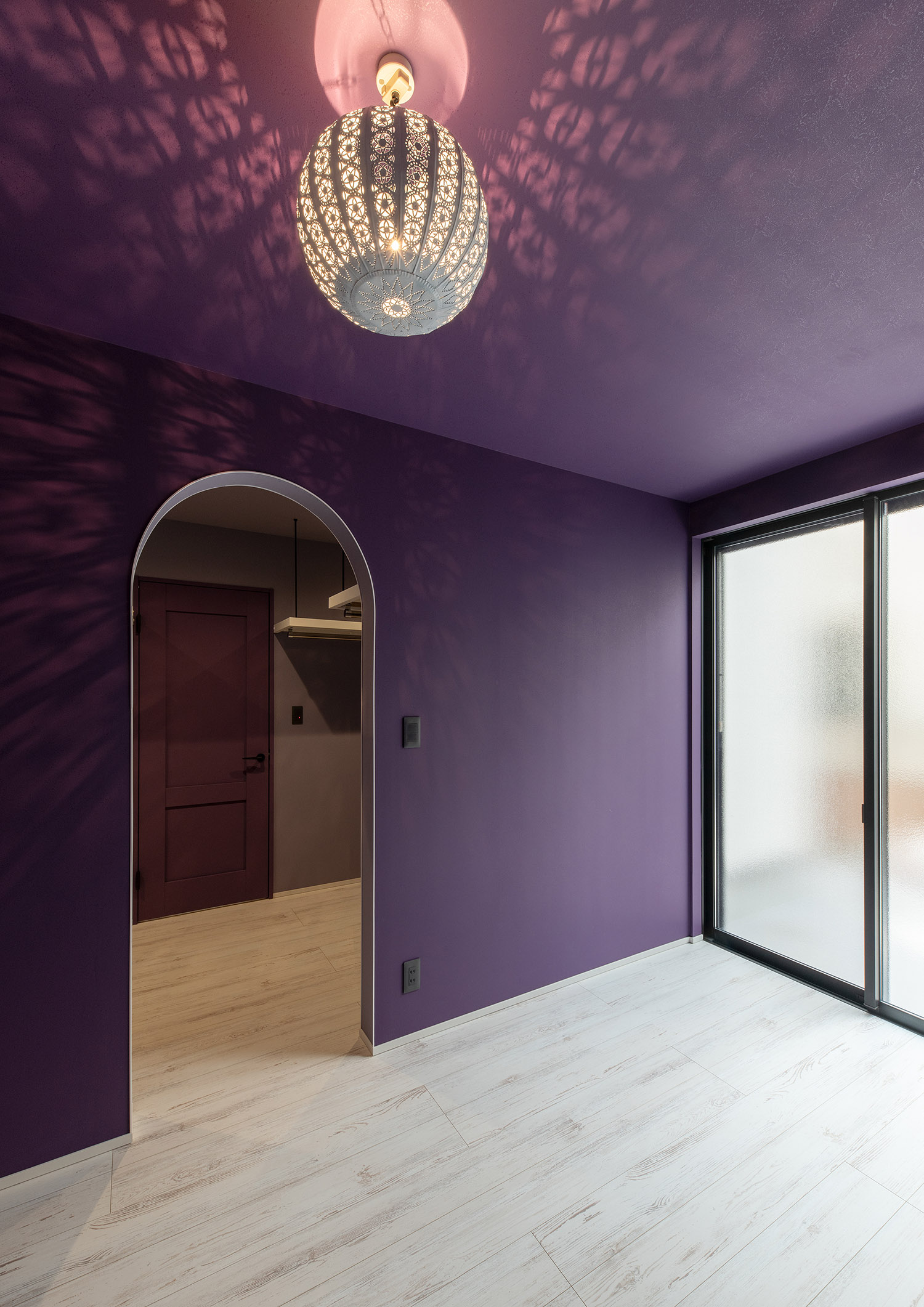 アーチ壁の入口で、紫のクロスにモザイクランプを取り付けた部屋・デザイン住宅