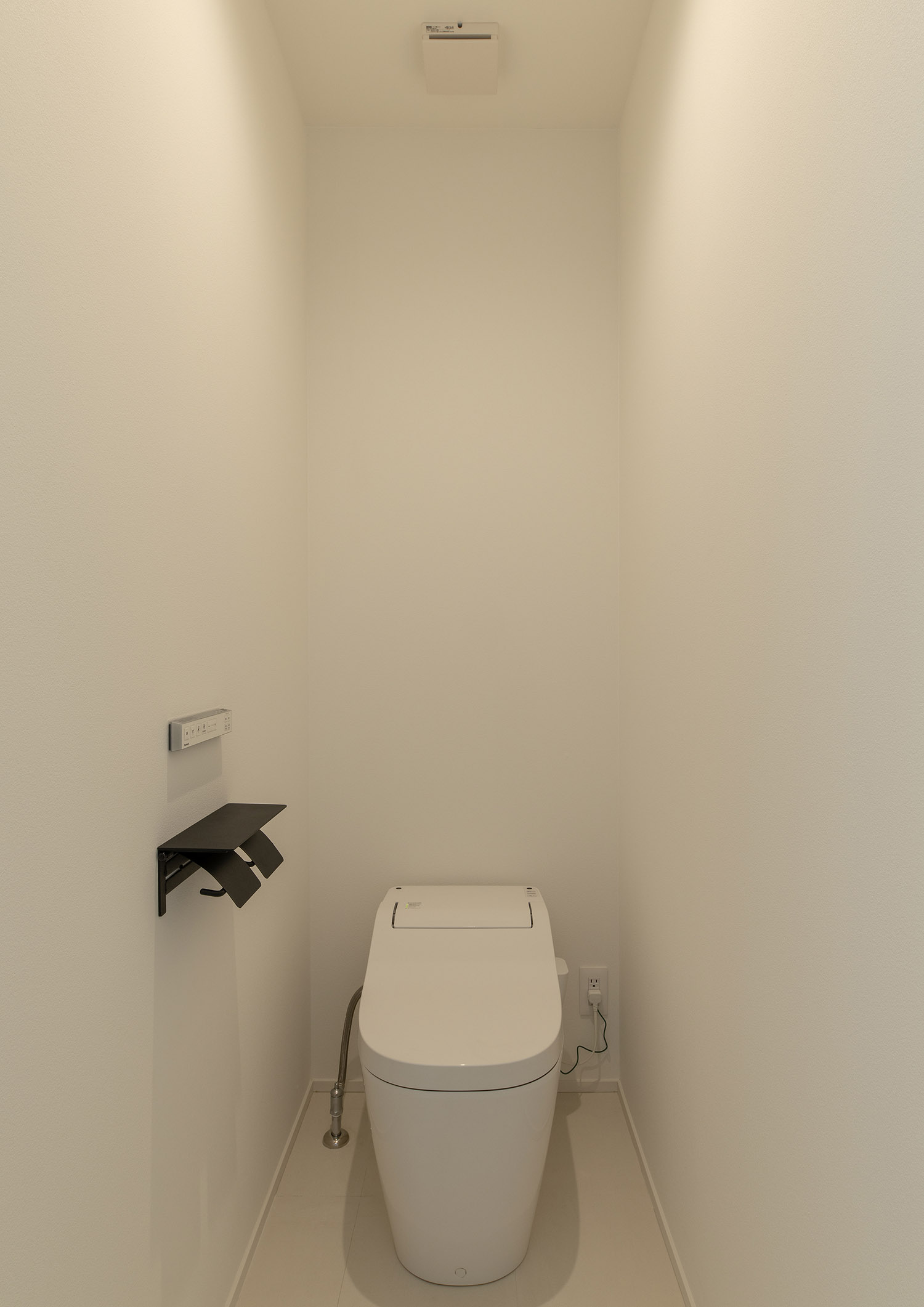 白い壁に囲まれた、黒いトイレットペーパーホルダーがあるトイレ・デザイン住宅