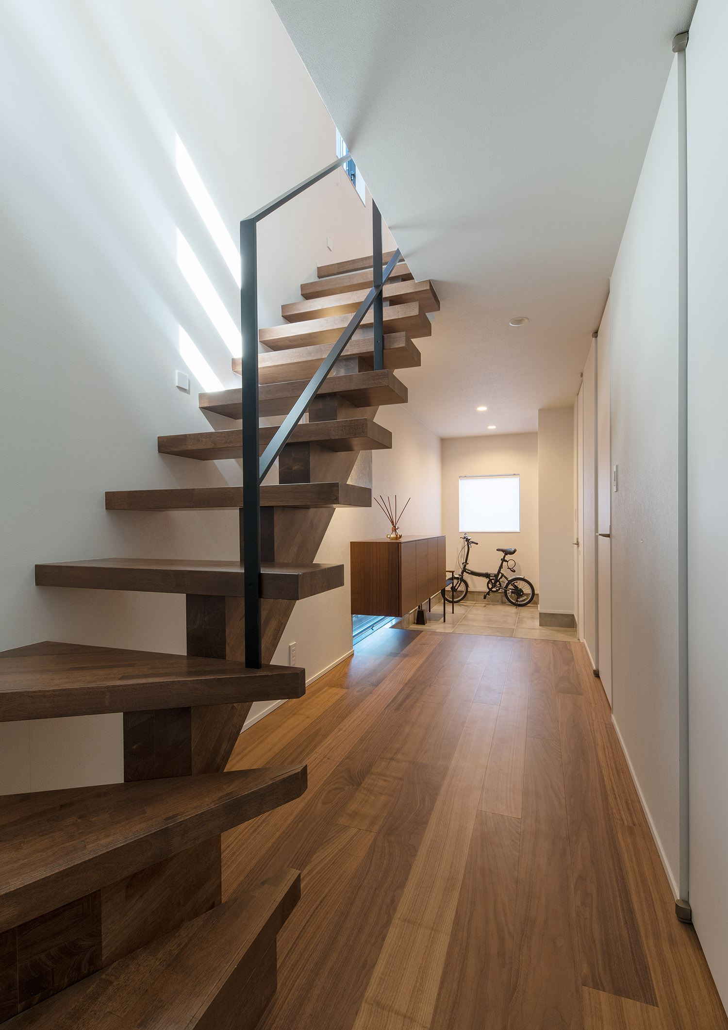 玄関と一直線に繋がる、木のスケルトン階段がある廊下・デザイン住宅