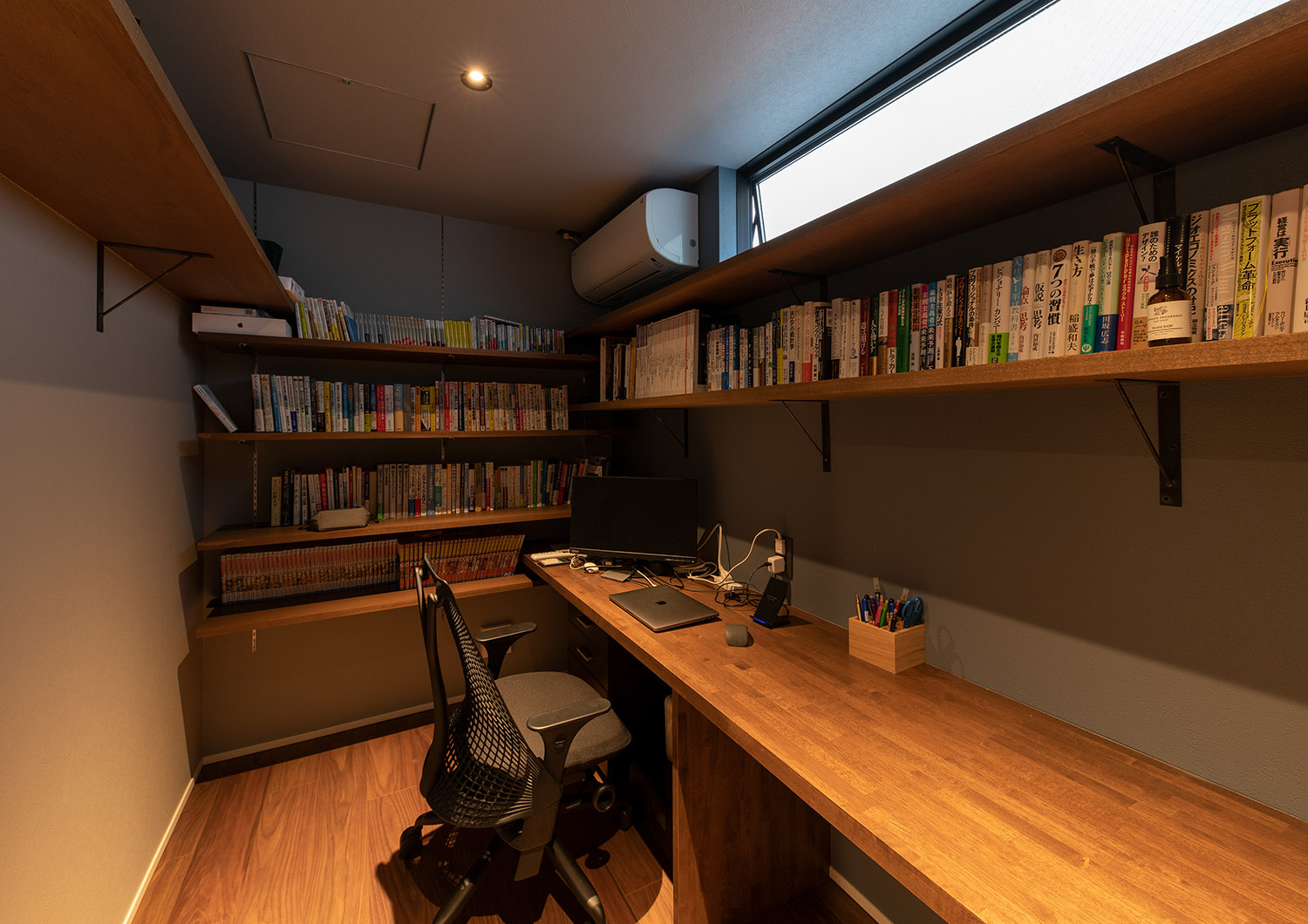 壁付けのデスクと本棚がある、ハイサイドライトから光が入る書斎・デザイン住宅