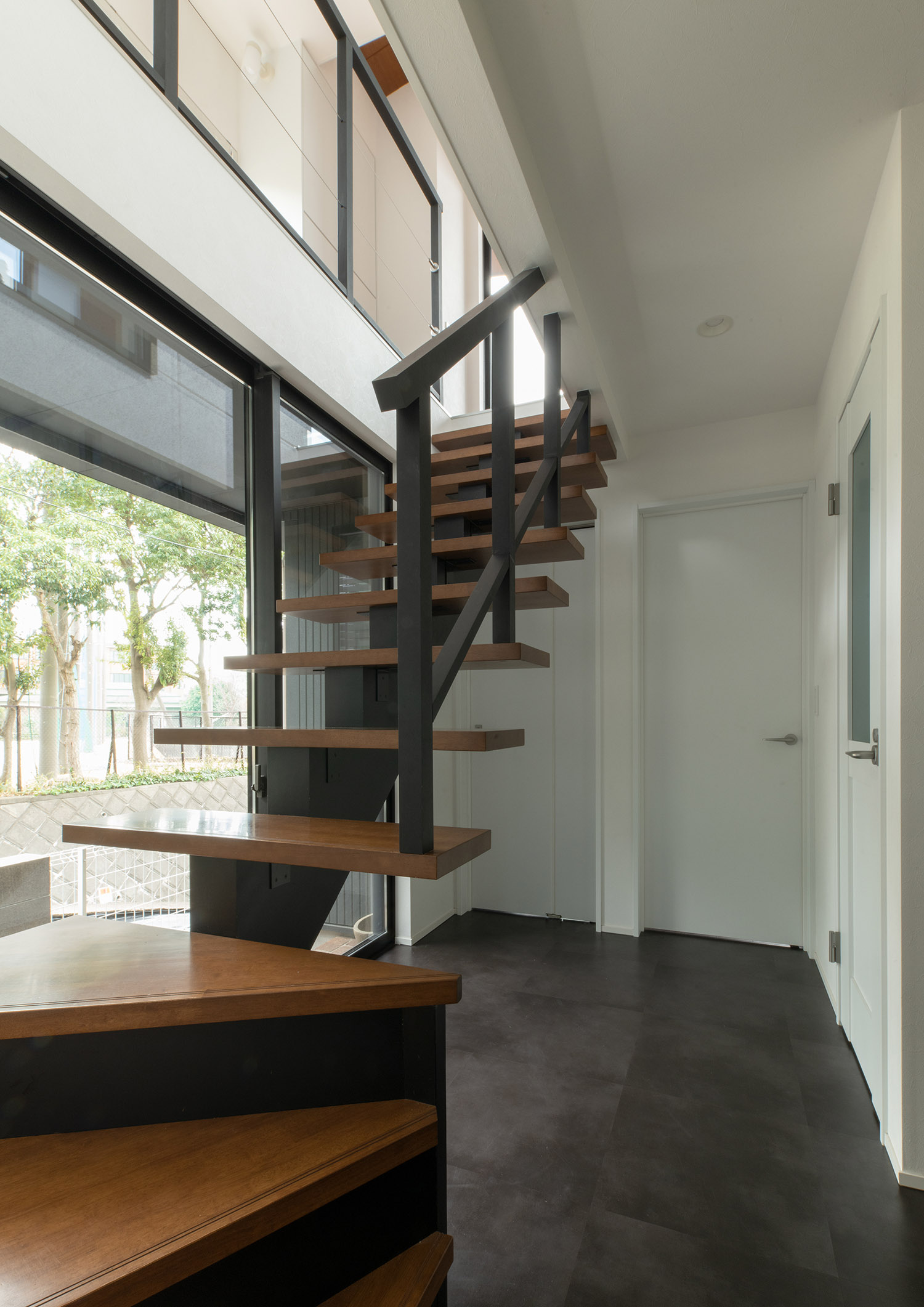白い壁と黒い床の空間にある木製のスケルトン階段・デザイン住宅