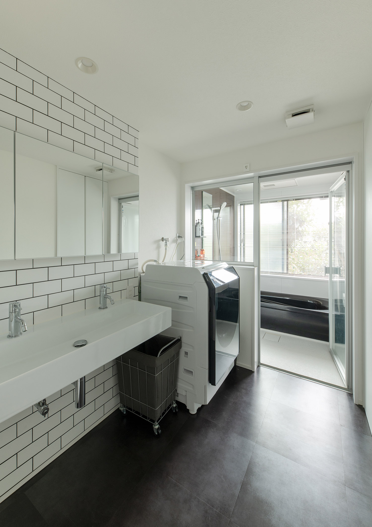 白を基調としたタイルのある洗面所の先にある浴室・デザイン住宅