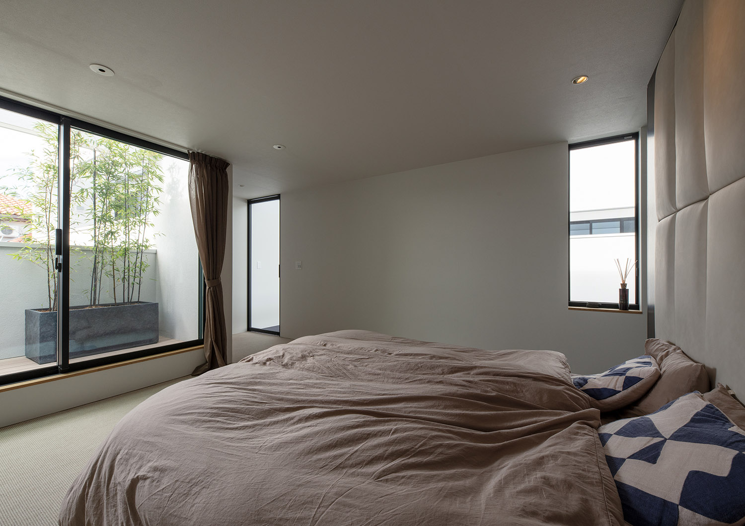 ベッドから植栽が置かれたバルコニーが見える寝室・デザイン住宅