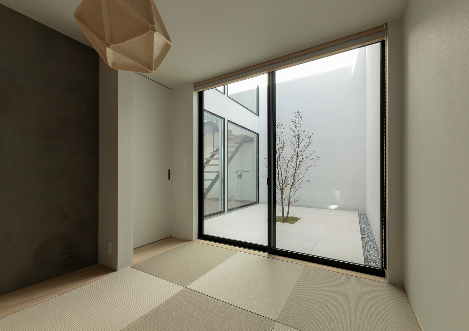 目隠し壁に囲まれた、植栽のある中庭が見える琉球畳の和室・デザイン住宅