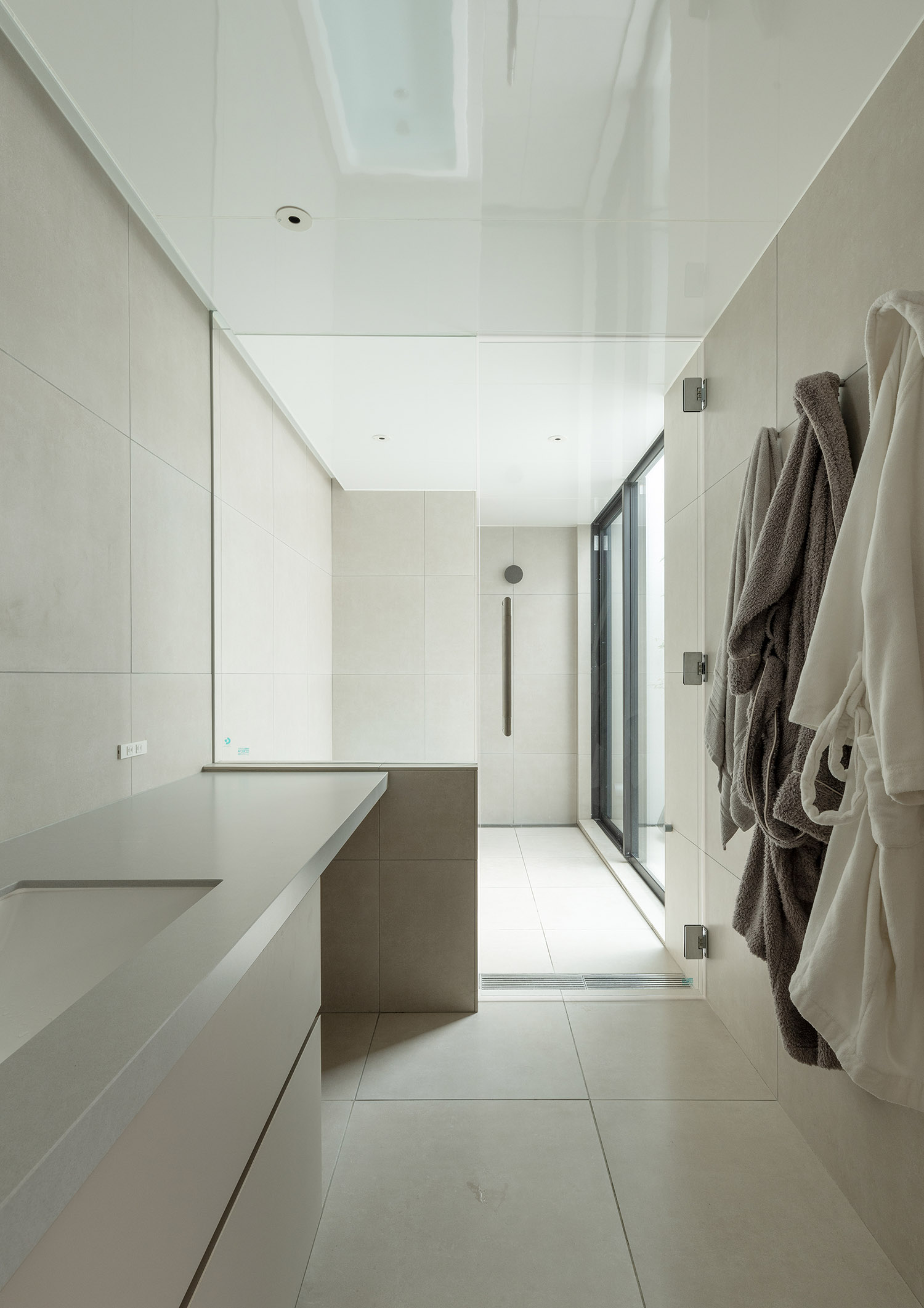 壁にバスローブが掛けられている洗面所と、ガラス扉で仕切られた浴室・デザイン住宅