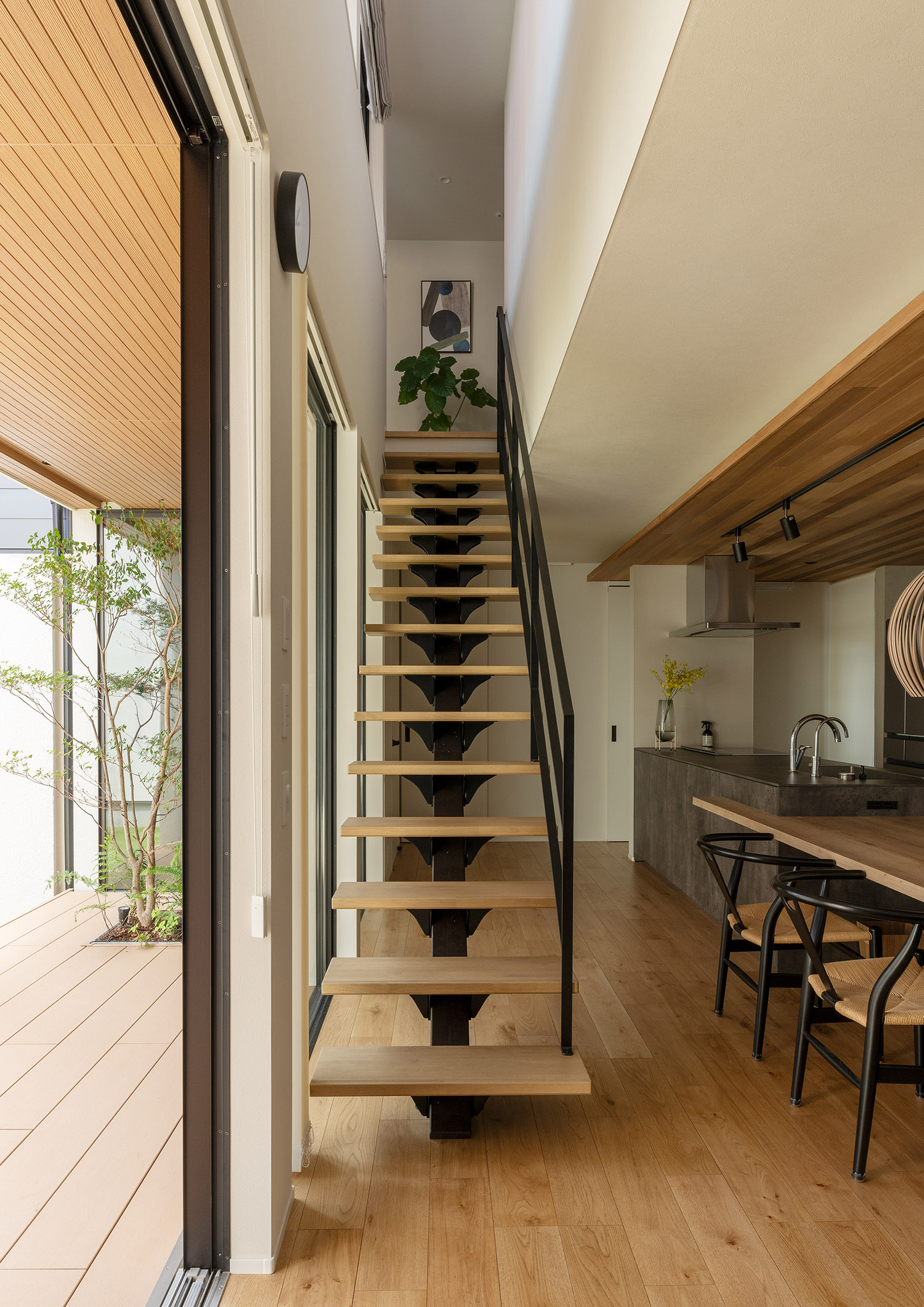 階段を上がった先に観葉植物やアートが飾られた木製のスケルトン階段・デザイン住宅