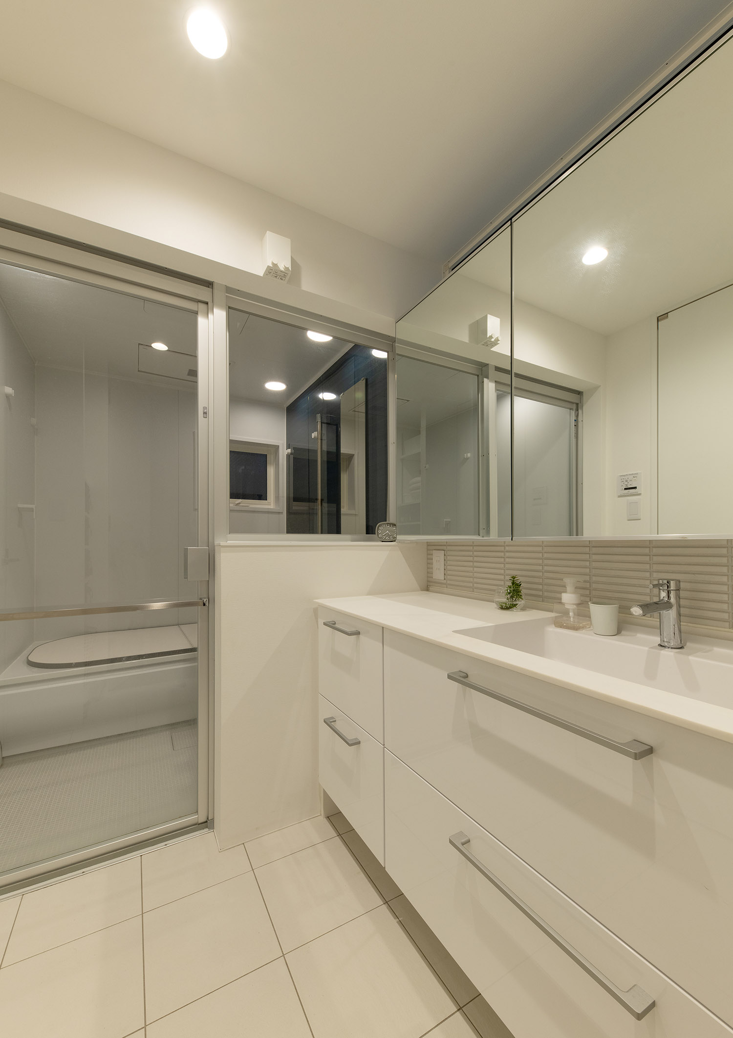 浴室とガラス扉で仕切られた白を基調とした明るい洗面所・デザイン住宅