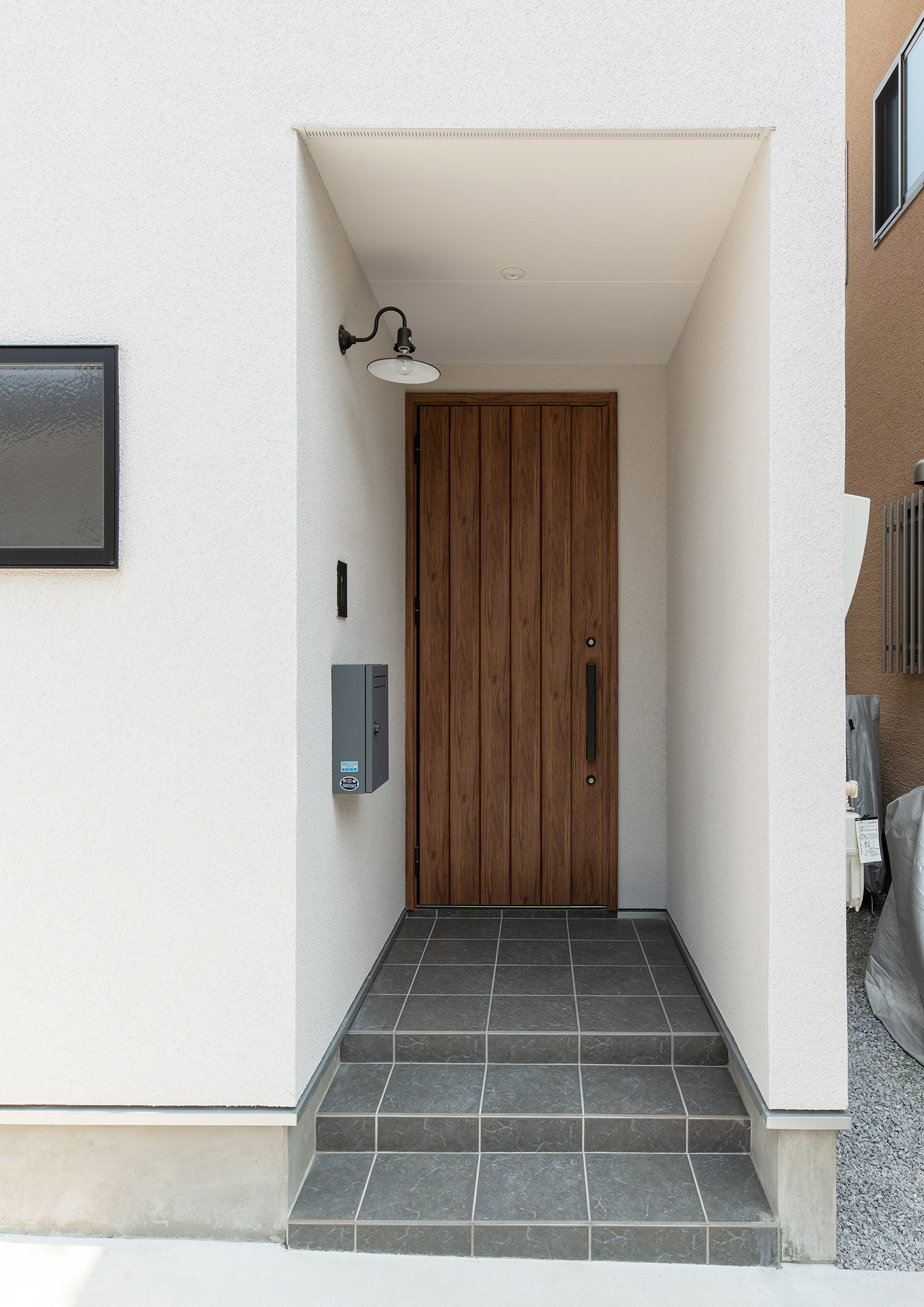 白い外壁に木の玄関扉を取り付けたシンプルな玄関ポーチ・デザイン住宅
