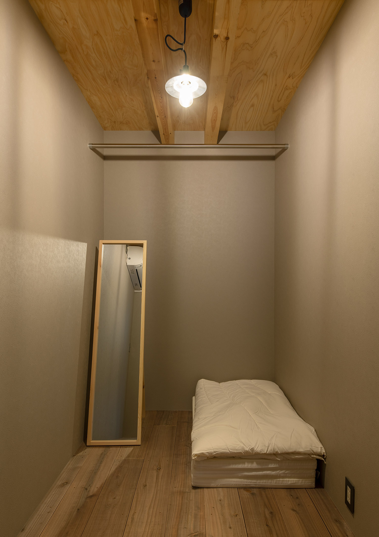 木の天井に布団と鏡を置いたシンプルな寝室・デザイン住宅