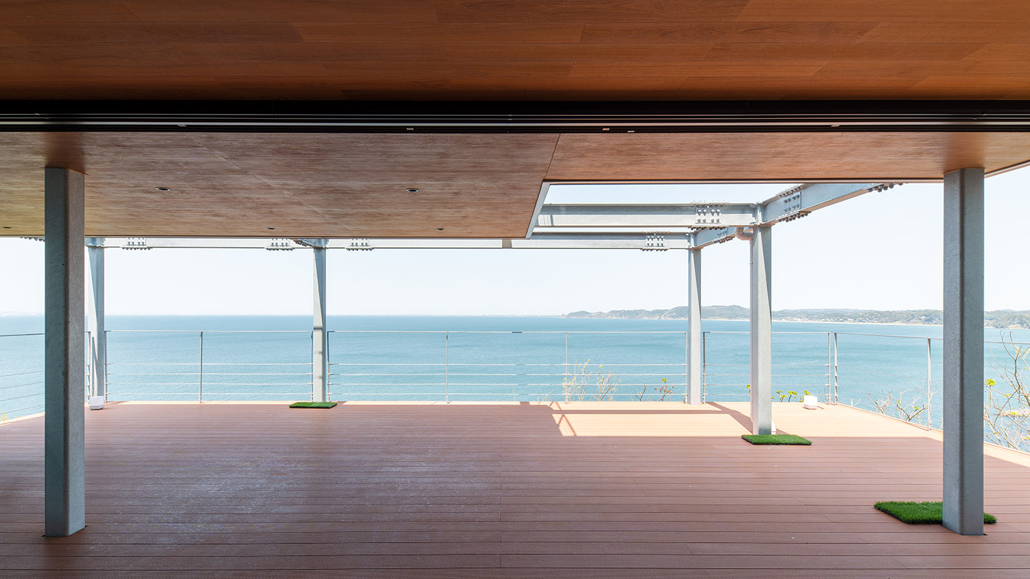 海と繋がるように見える屋根付きのウッドデッキのテラス・デザイン住宅