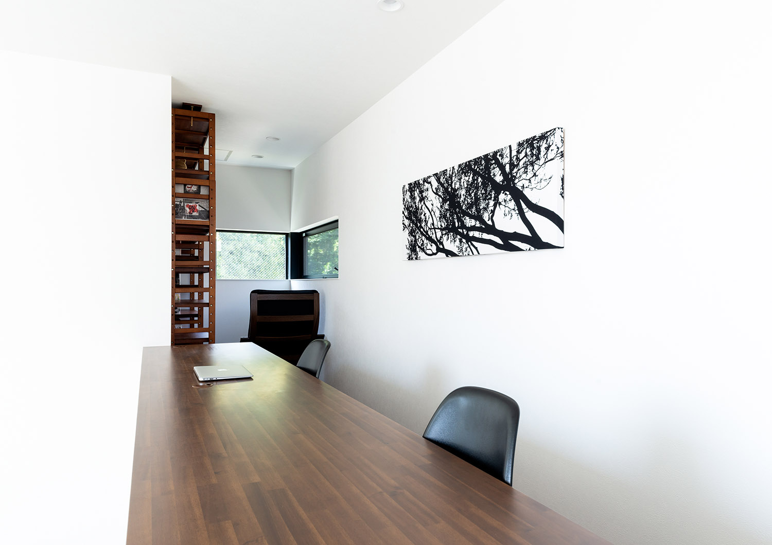 壁にモノクロのアートが飾られた木のデスクがある書斎・デザイン住宅
