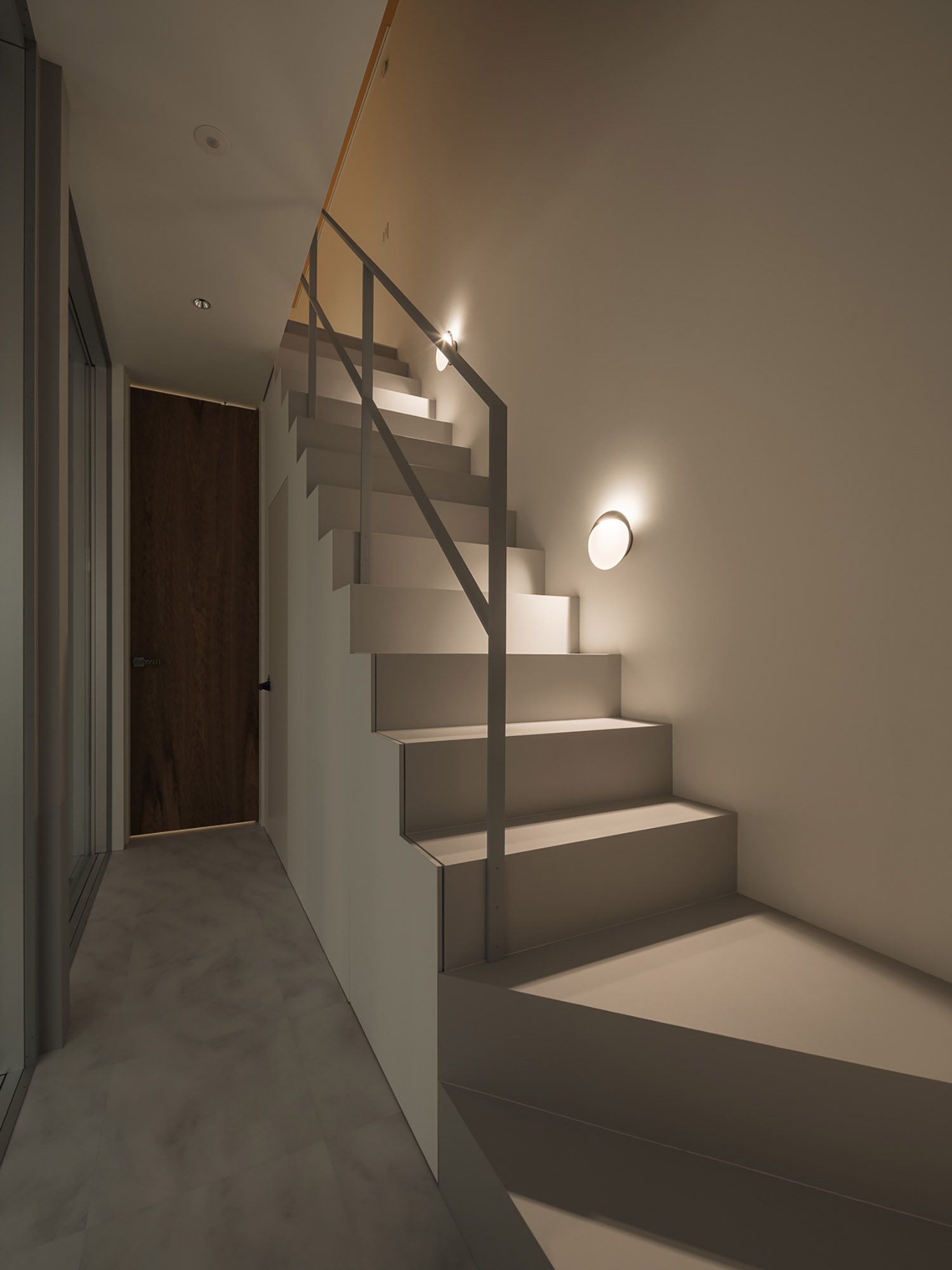 壁に間接照明を取り付けた白い箱型階段・デザイン住宅