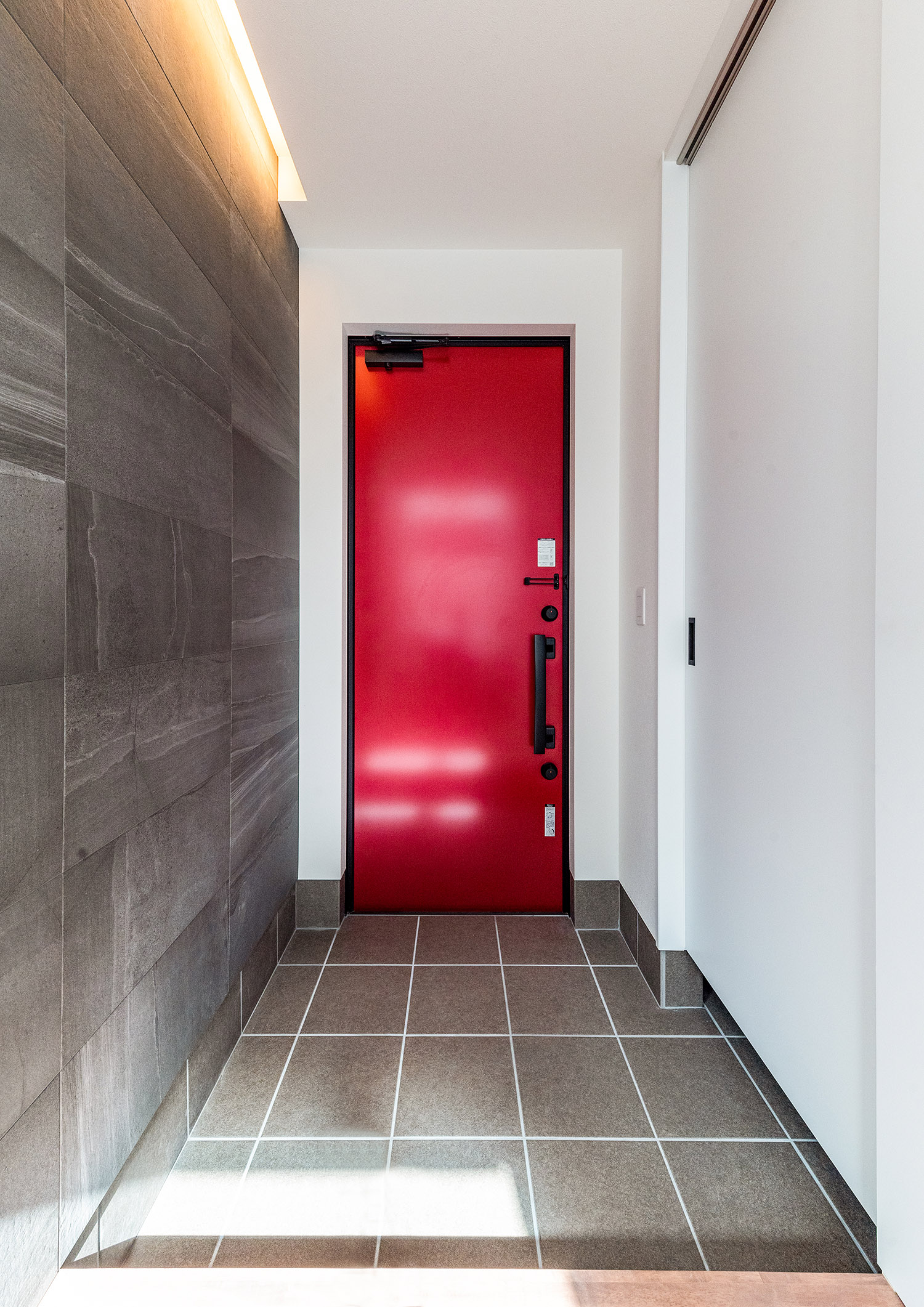 グレーの床と壁の玄関で赤い扉がアクセントになった玄関・デザイン住宅