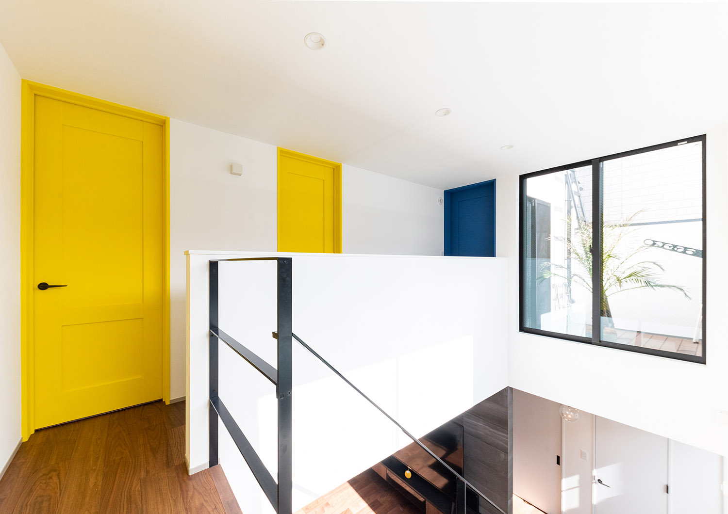 白い壁に黄色や青の扉がアクセントになっている廊下・デザイン住宅