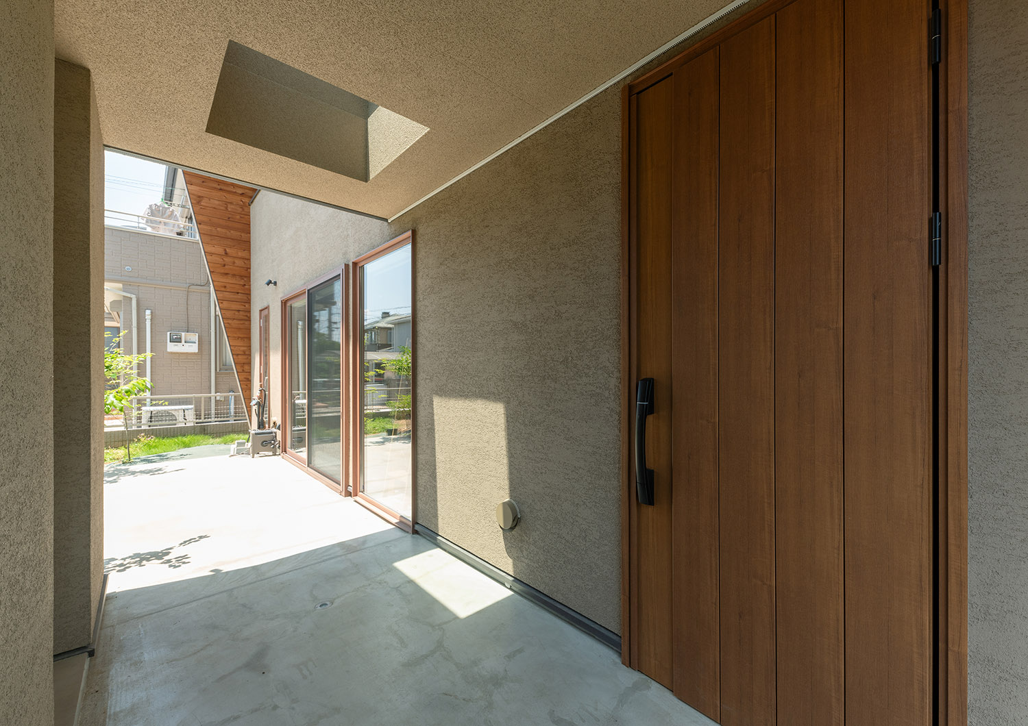 ベージュの塗り壁に木の玄関扉を取り付けたナチュラルなアプローチ・デザイン住宅