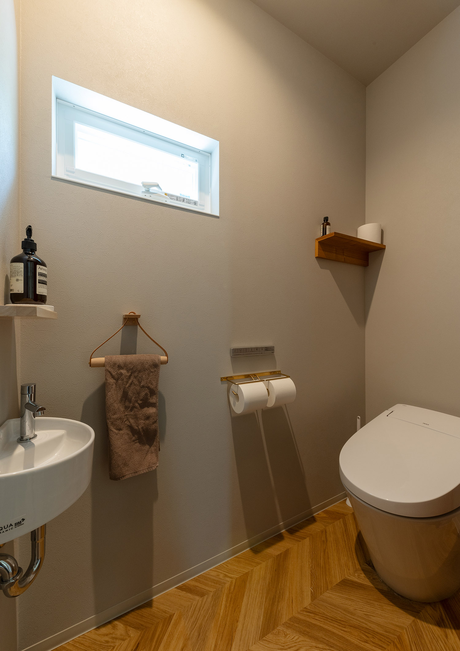 丸い薄型手洗いを取り付けたヘリンボーン床のトイレ・デザイン住宅