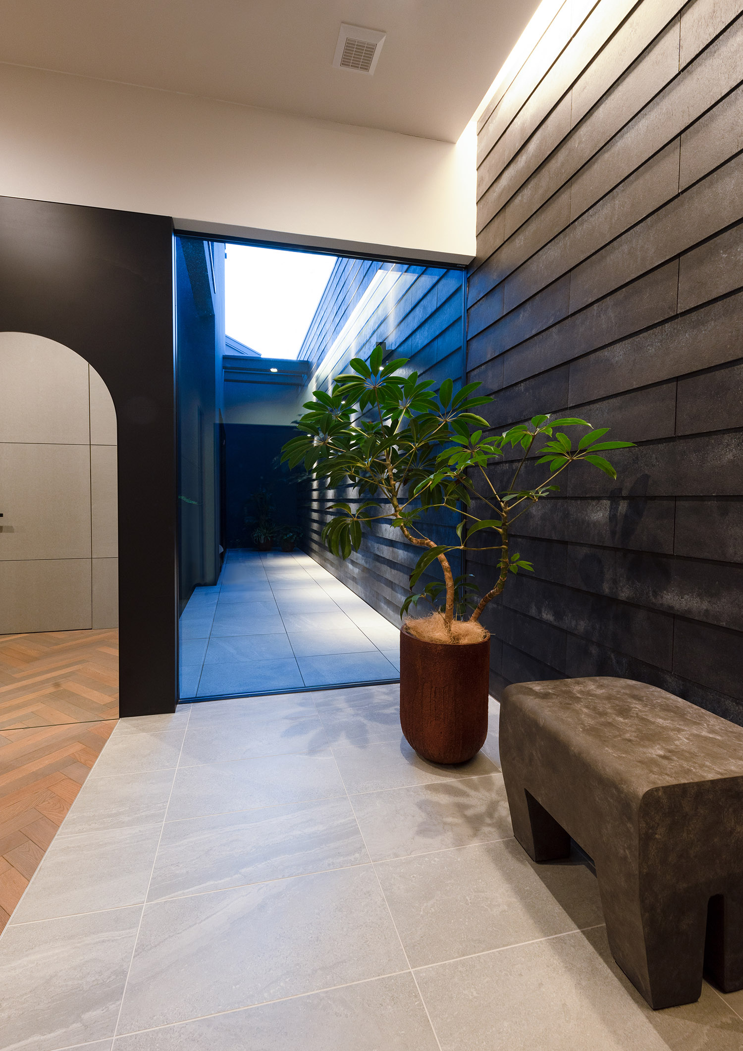 コンクリートのベンチや植栽がある、壁際に間接照明を取り付けたおしゃれな玄関・デザイン住宅