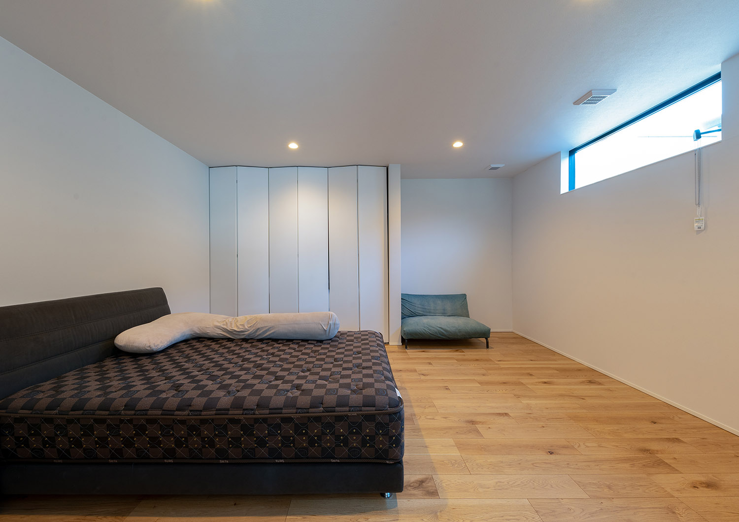 天井近くにスリット窓を取り付けたプライバシーが確保されたシンプルな寝室・デザイン住宅
