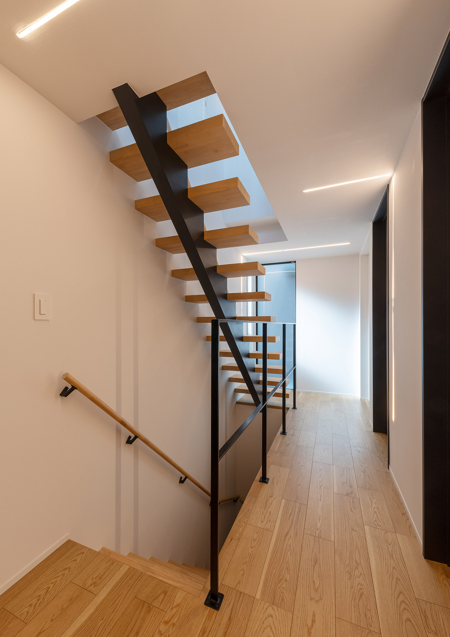 吹き抜けの階段室のそばにある、黒いアイアンの手すりを取り付けた廊下・デザイン住宅