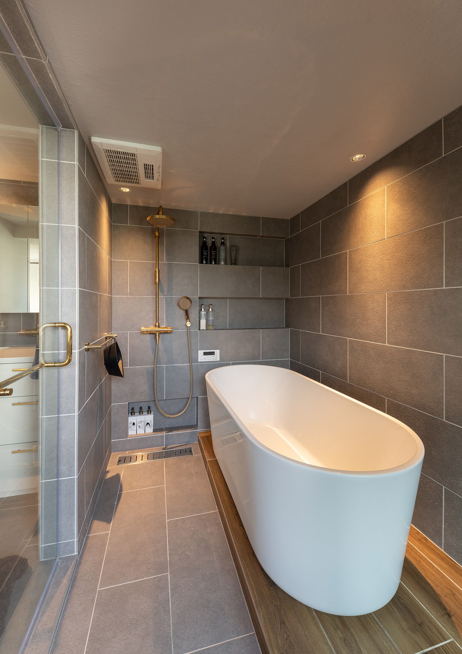 グレーの壁で洗面所との繋がりが感じられる丸い浴槽がある在来浴室・デザイン住宅
