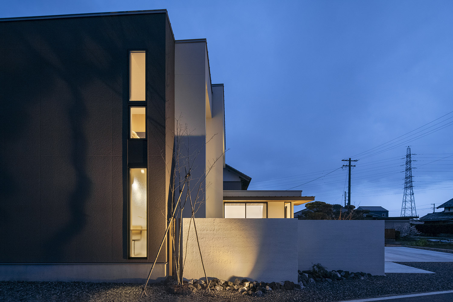 白い目隠し壁が照明に照らされるモノトーンの外観の家・デザイン住宅