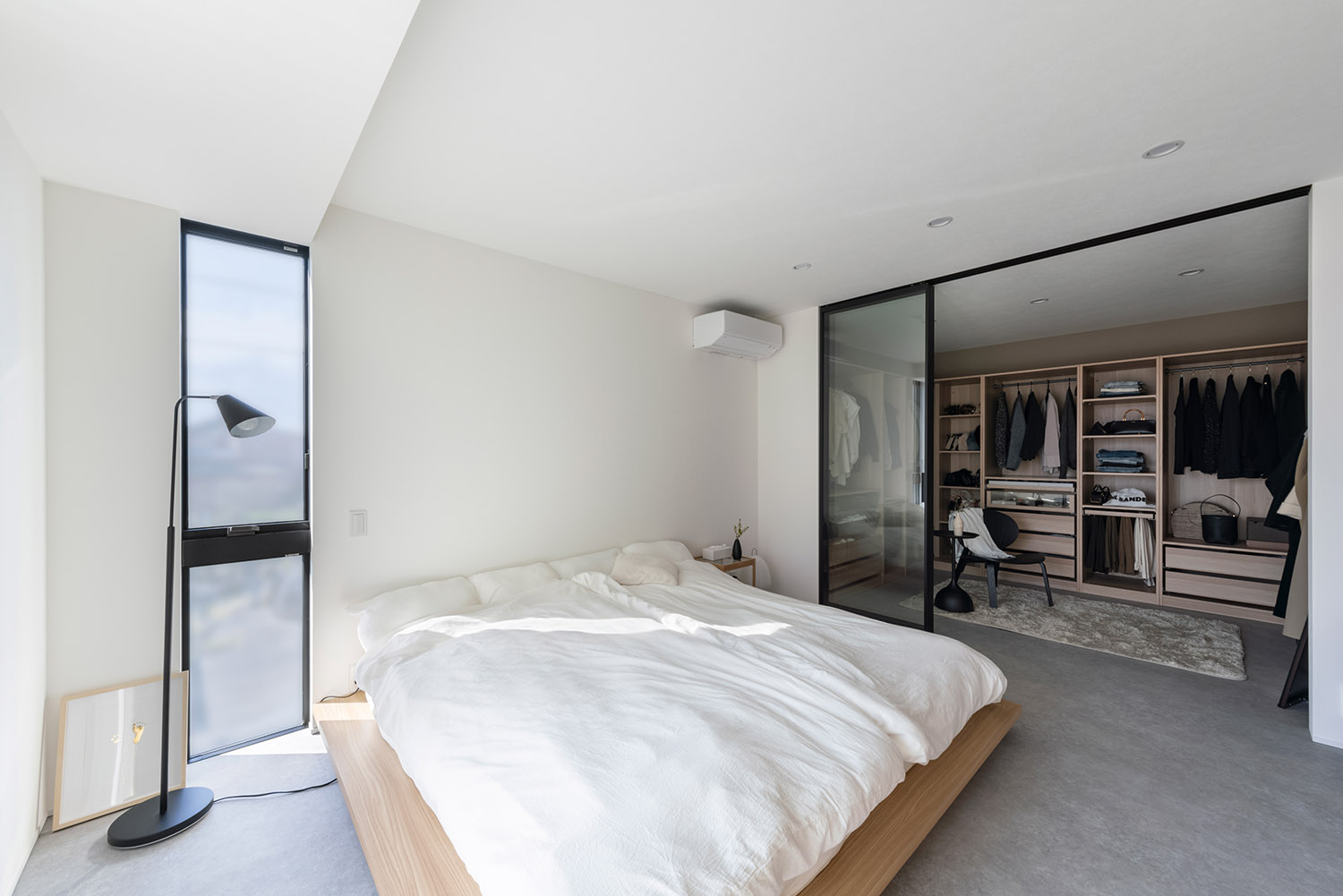 ガラス扉で仕切られたウォークインクローゼットがあるシンプルで広い寝室・デザイン住